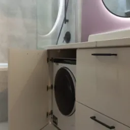 Nowoczesna łazienka z pralką ukrytą w szafce pod umywalką, okrągłe lustro z podświetleniem LED, kabina prysznicowa z czarną armaturą.