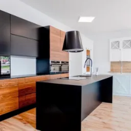 Nowoczesna kuchnia na wymiar: czarne szafki górne, drewniane dolne, wyspa z czarnym blatem, okap tubowy. Ekspozycja w salonie meblowym.