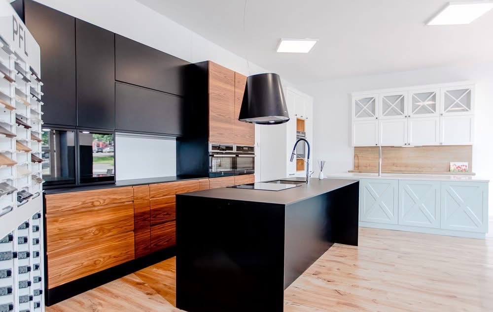 Nowoczesna kuchnia na wymiar: czarne szafki górne, drewniane dolne, wyspa z czarnym blatem, okap tubowy. Ekspozycja w salonie meblowym.