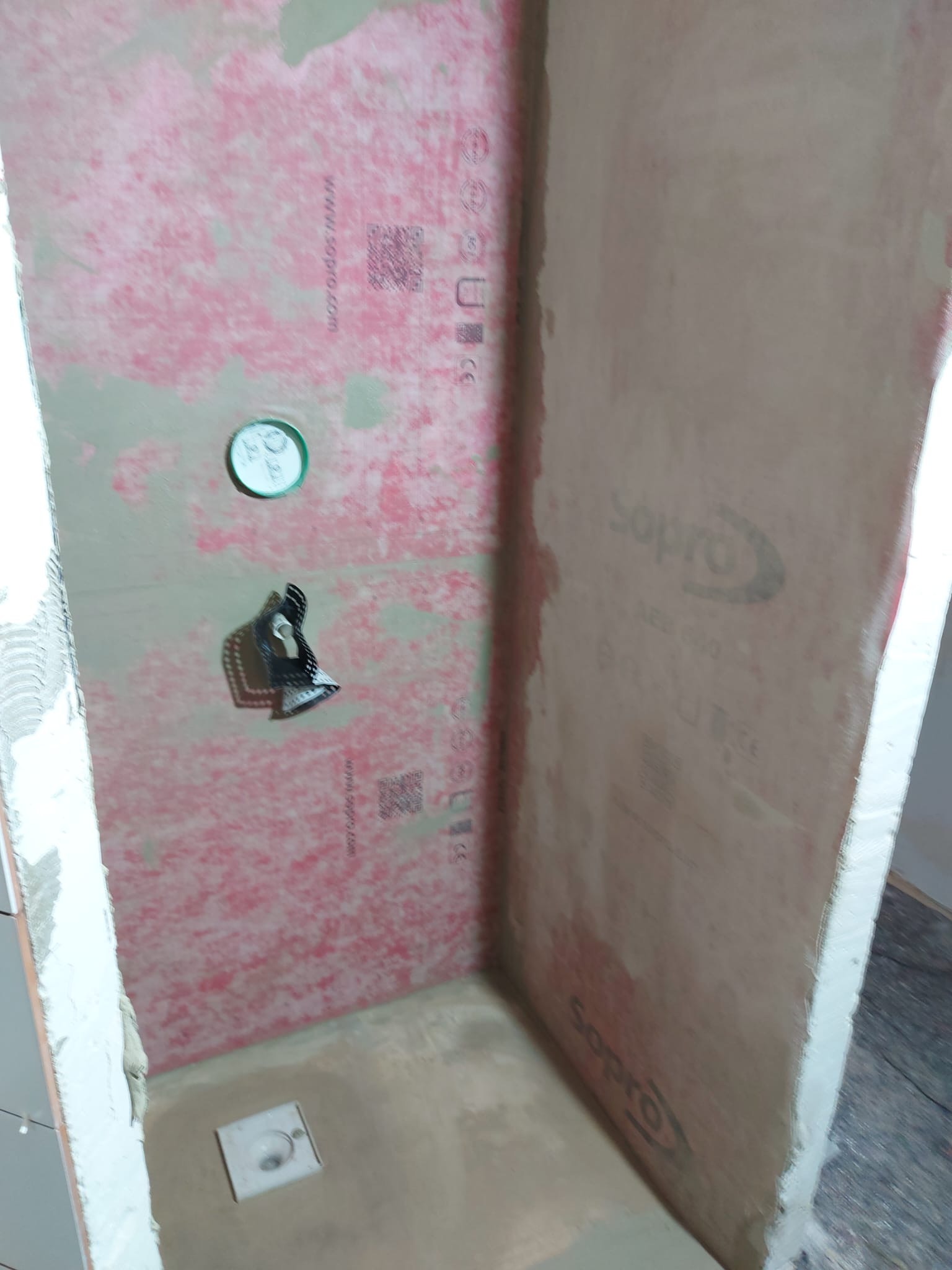 Przygotowana strefa prysznicowa z zamontowaną izolacją przeciwwodną Sopro na ścianach, widoczny odpływ liniowy w podłodze i przygotowane miejsce na baterię.