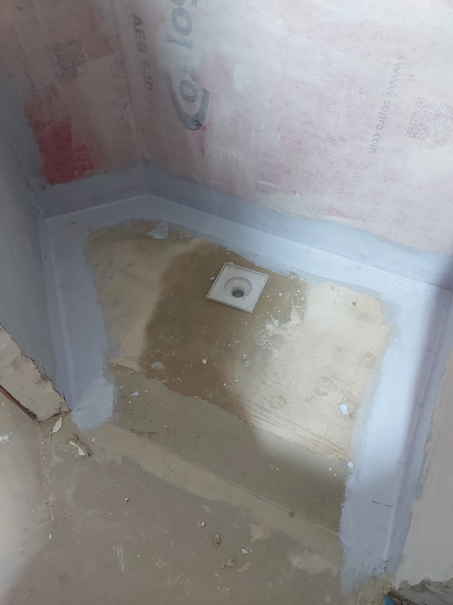 Przygotowanie podłoża w kabinie prysznicowej: hydroizolacja ścian z widocznym logo Sopro i odpływ liniowy przed położeniem płytek.