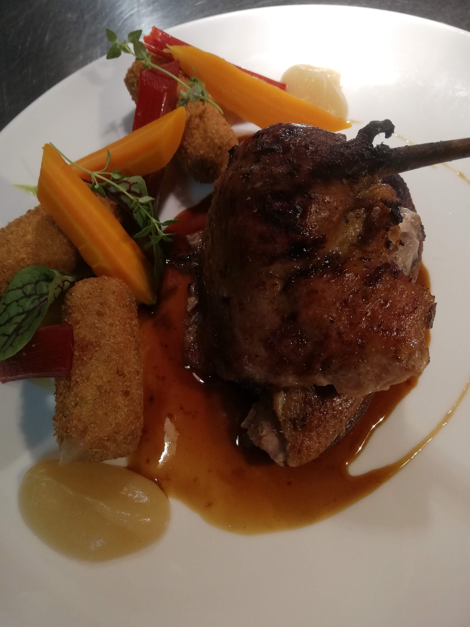 Elegancko podana pieczona noga kaczki z sosem, marchewką, krokietami i dekoracją z ziół na białym talerzu.