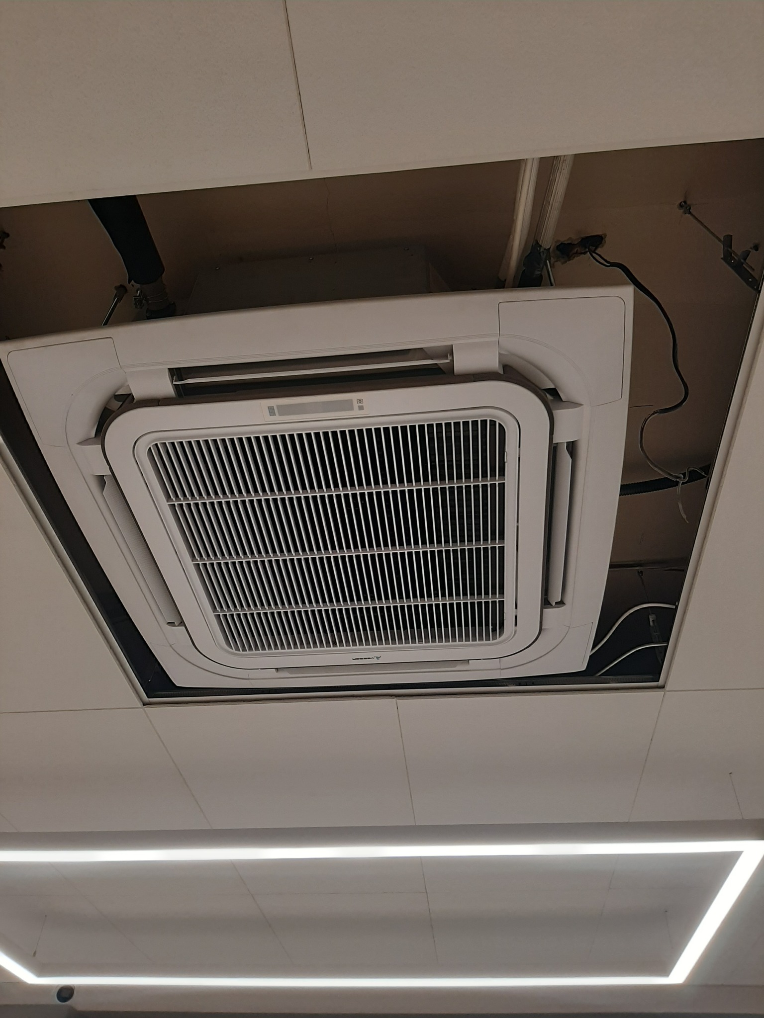 Kasetonowa jednostka klimatyzacji sufitowej zamontowana w podwieszanym suficie, widoczne przewody i elementy instalacji w Szubinie.