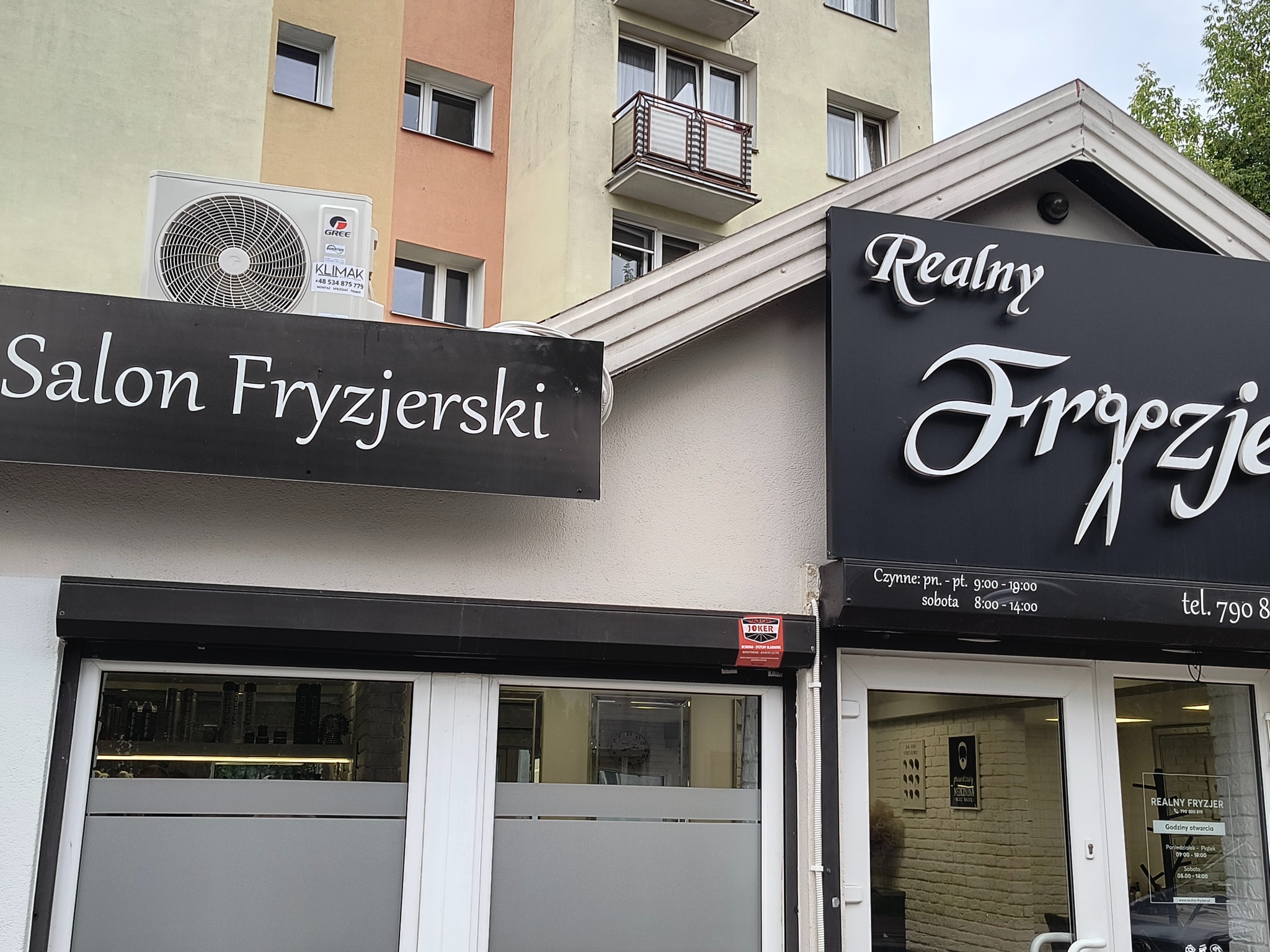 Dwa lokale fryzjerskie obok siebie z zamontowanymi roletami zewnętrznymi i klimatyzacją. Na fasadzie widoczne szyldy z nazwami salonów.