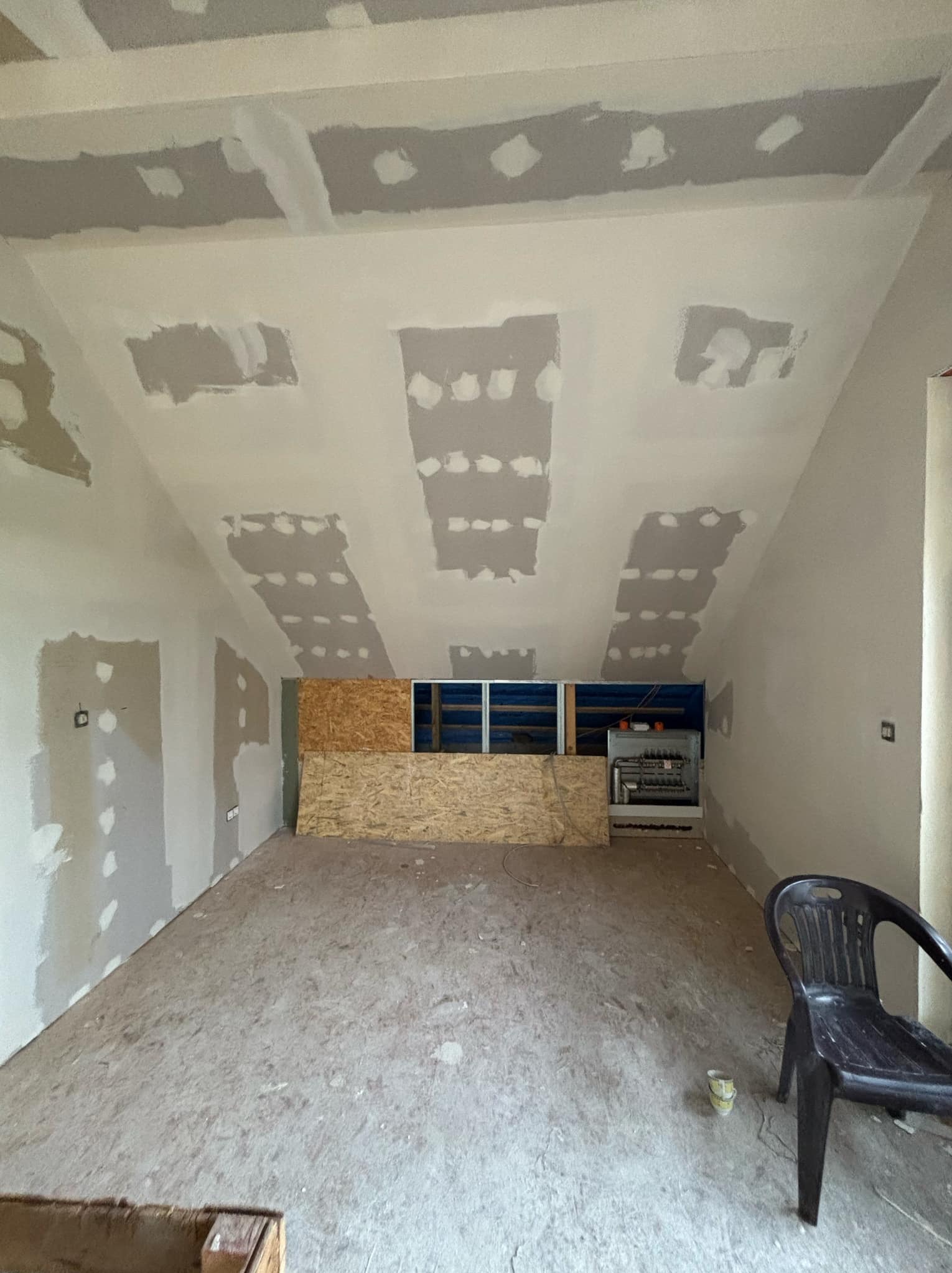 Poddasze w trakcie prac wykończeniowych: widoczne płyty kartonowo-gipsowe na suficie i ścianach, częściowo zaszpachlowane, z widocznymi łączeniami i śrubami. Na podłodze płyty OSB, w tle widoczne...