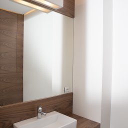 WEGA RAFAŁ ZYCH - Nowoczesna łazienka z umywalką nablatową, lustrem z podświetleniem LED i okładziną z drewna orzechowego.