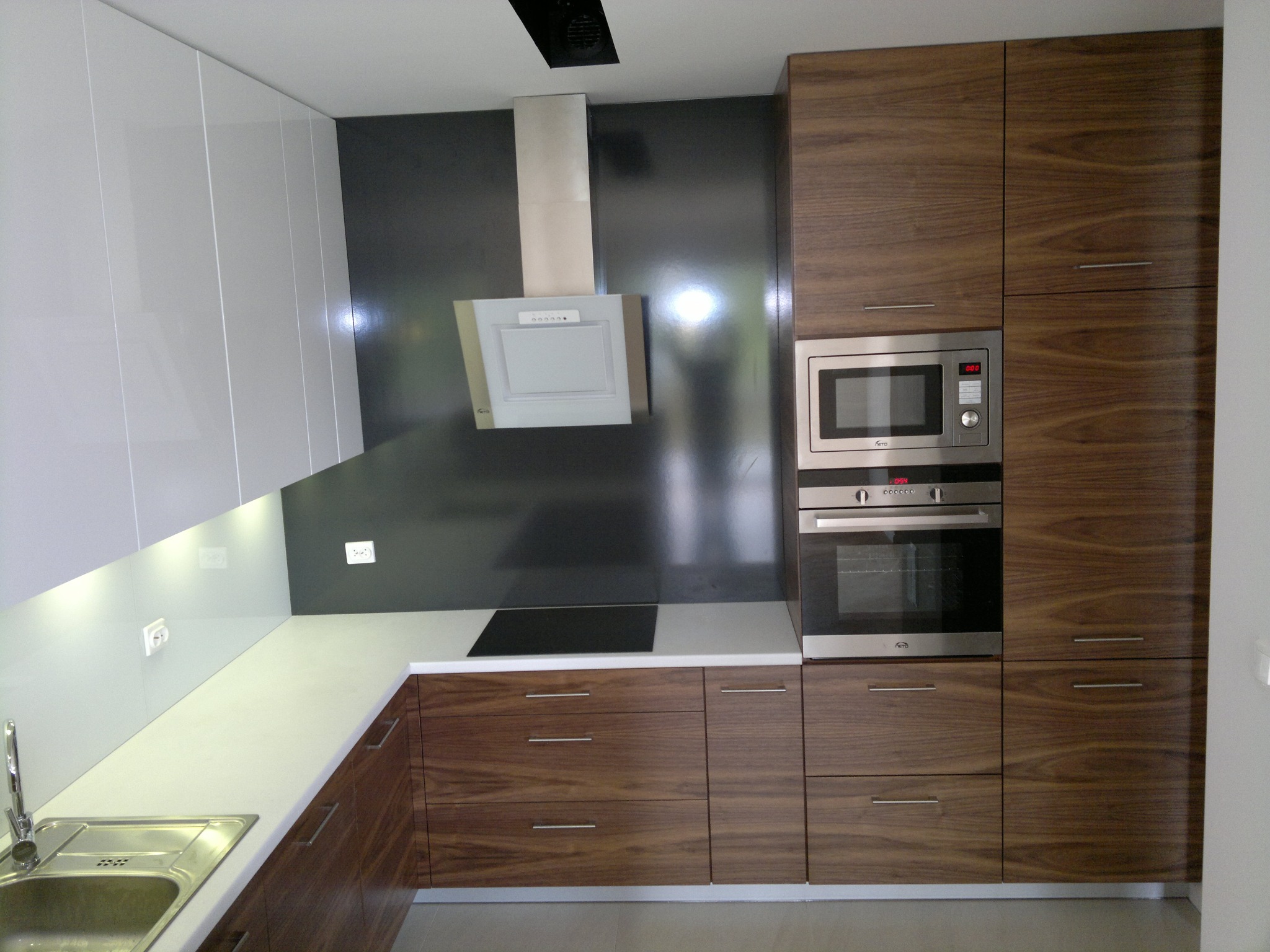 Nowoczesna kuchnia z białymi, lakierowanymi szafkami górnymi i drewnianymi szafkami dolnymi z wyraźnym usłojeniem, wyposażona w sprzęt AGD w zabudowie i czarną płytę indukcyjną.