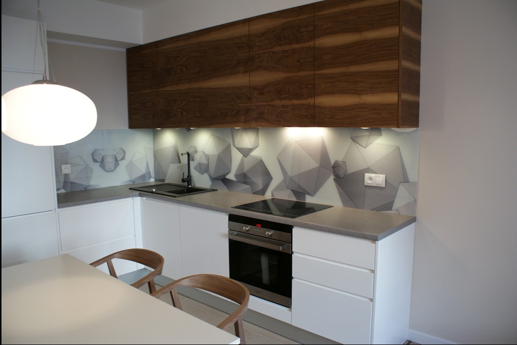 Nowoczesna kuchnia z białymi szafkami, drewnianymi górnymi szafkami i geometrycznym wzorem na szklanym panelu nad blatem, oświetlona lampą wiszącą.