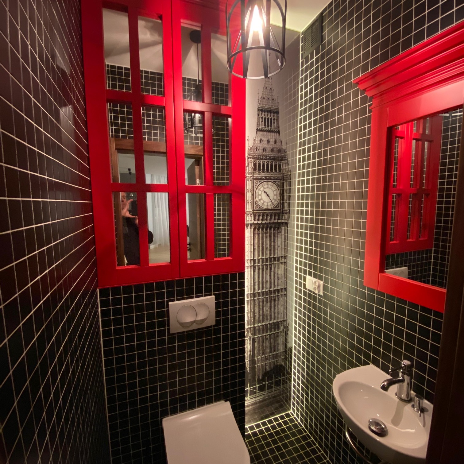 Nietypowa aranżacja małej łazienki z czarną mozaiką, czerwonymi akcentami w postaci ramy lustra i okna, oraz fototapetą z motywem Big Bena.