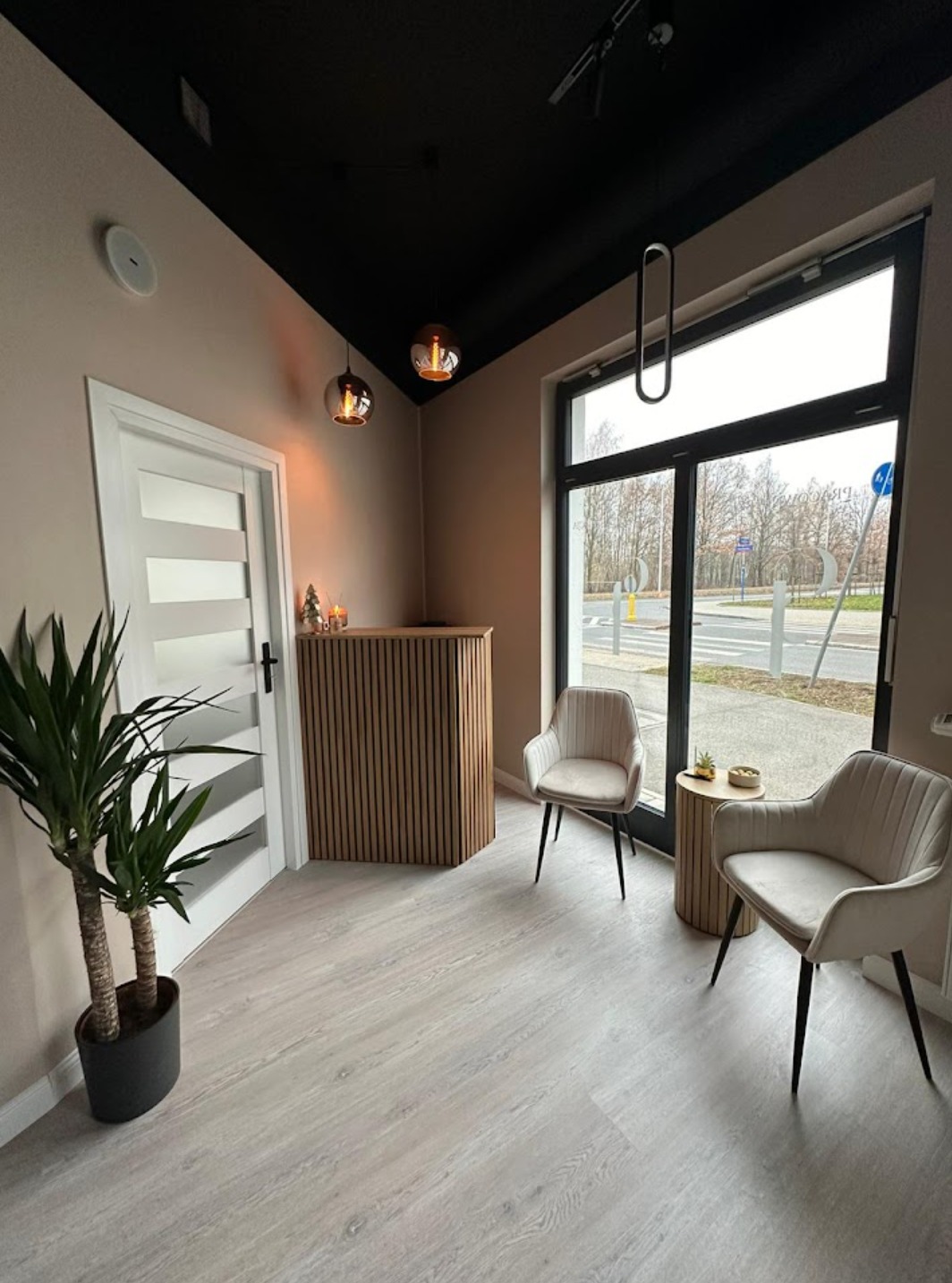 Nowoczesne wnętrze biura z recepcją wykończoną drewnianymi lamelami, dwoma krzesłami obitymi beżowym welurem, stolikiem pomocniczym i dużym oknem z widokiem na ulicę. Na podłodze jasne panele...