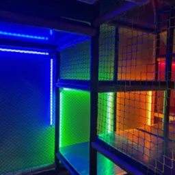 Wielopoziomowa konstrukcja zabawowa z siatki, oświetlona różnokolorowymi diodami LED: niebieskim, zielonym, pomarańczowym i czerwonym.