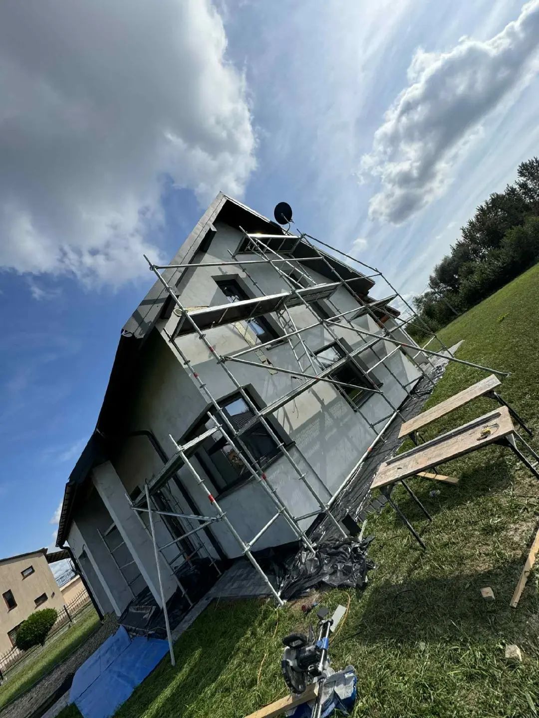 Dom w trakcie ocieplania elewacji, widoczne rusztowania, ocieplenie i narzędzia. Ujęcie z dołu, niebo z chmurami w tle.