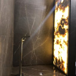 BUMAR Mariusz Ambroży - Nowoczesna łazienka wykończona włoskim marmurem w płytach, z podświetlonym panelem z onyksu i minimalistyczną, chromowaną baterią podłogową.