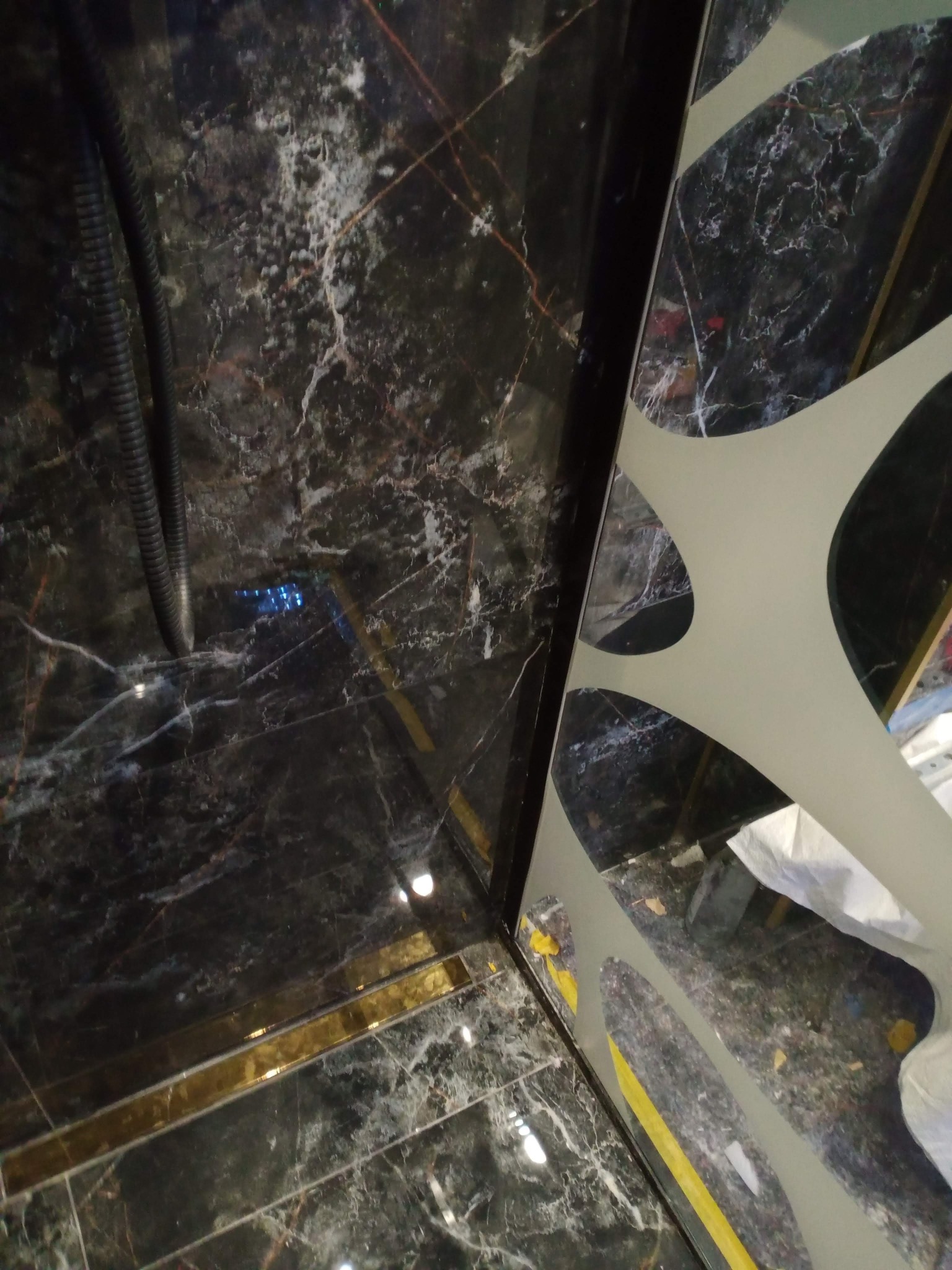 Czarny marmur z złotymi akcentami w kabinie prysznicowej, widoczna szyba z wzorem i przewód instalacji. Nietypowe ujęcie z góry.