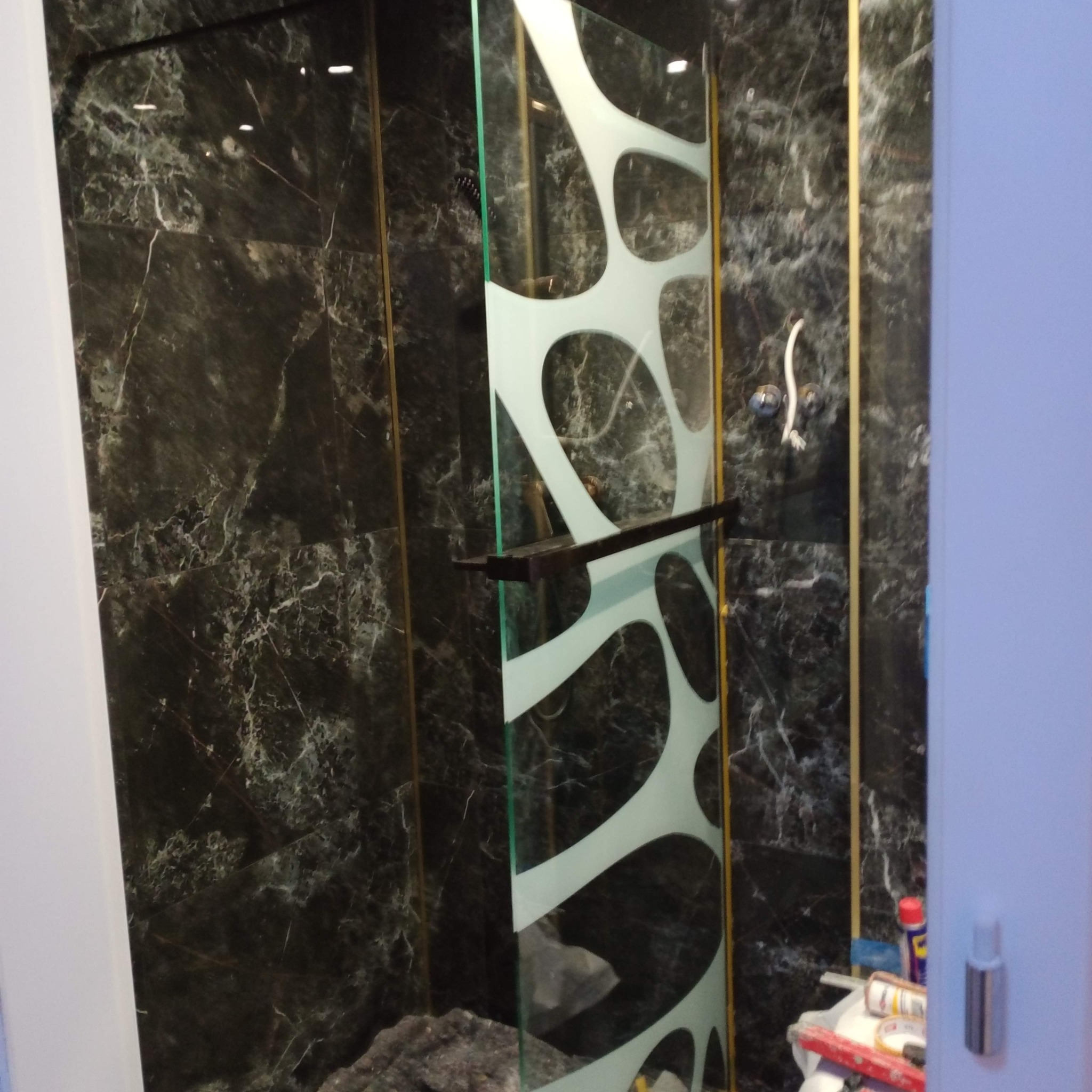 Kabina prysznicowa z czarnymi marmurowymi płytkami i dekoracyjną, matową szybą. Widoczne narzędzia i chemia, co sugeruje prace wykończeniowe.