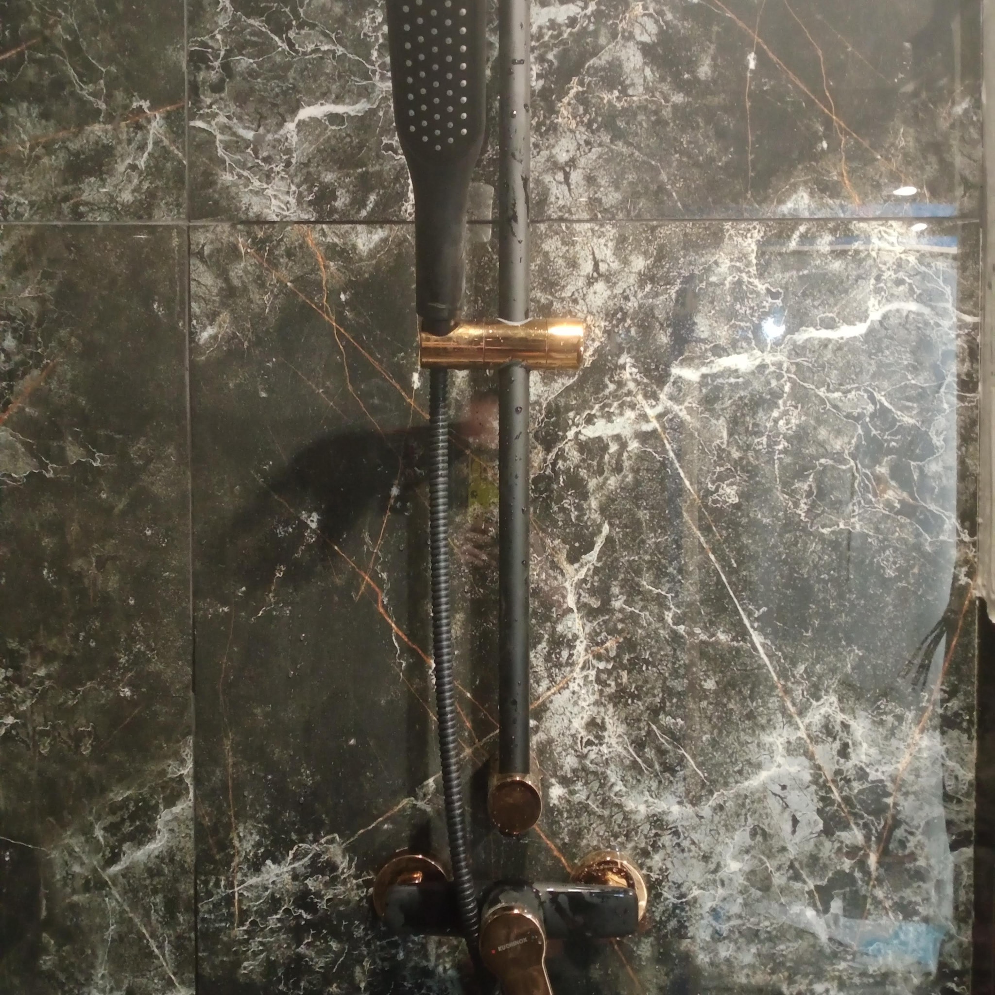 Czarno-złota bateria natryskowa na tle marmurowych płytek. Widoczne krople wody, podkreślające świeżość i nowoczesny design.