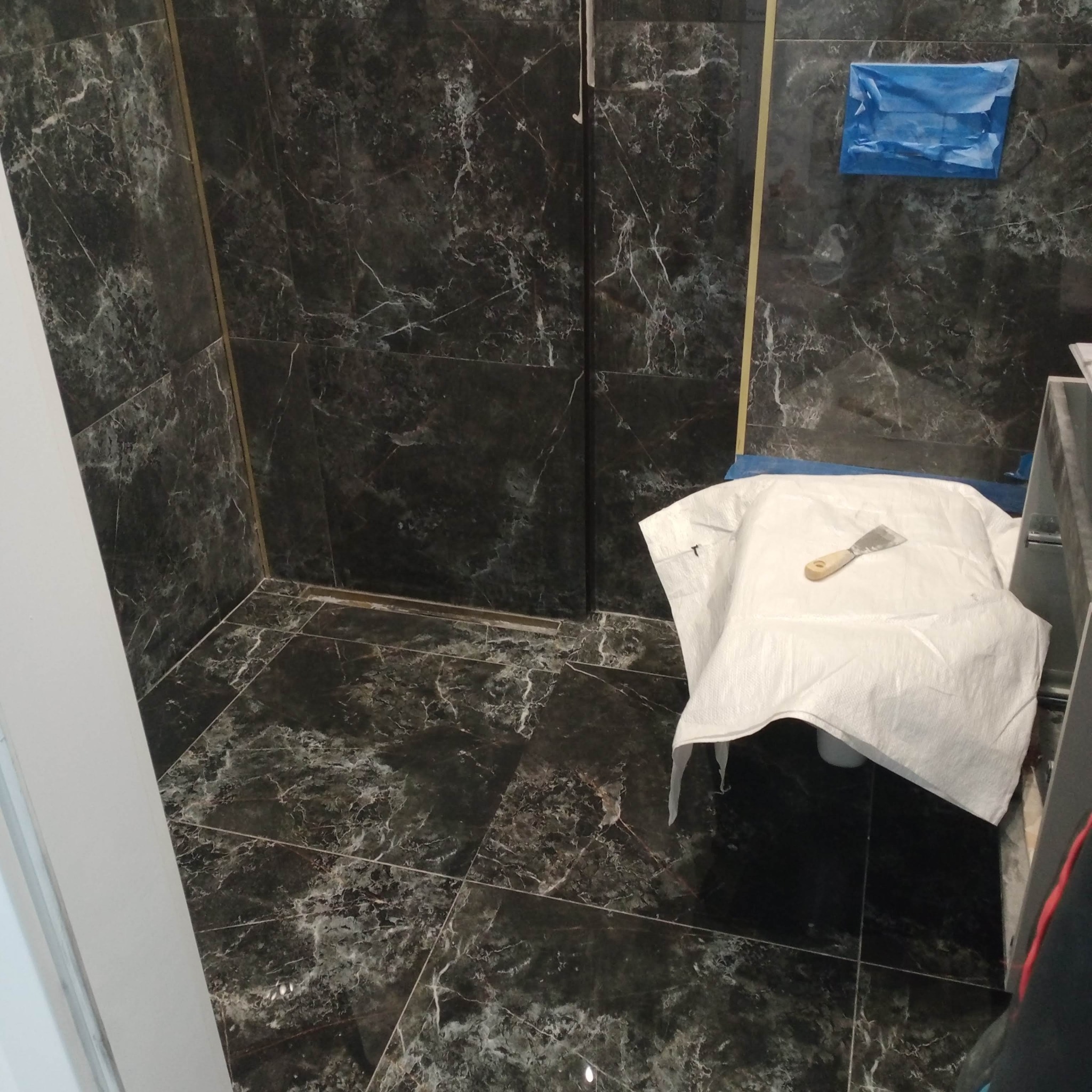 Wykończona łazienka z czarnymi płytkami imitującymi marmur. Na podłodze widoczny odpływ liniowy, a na sedesie leży biała plandeka z narzędziem.