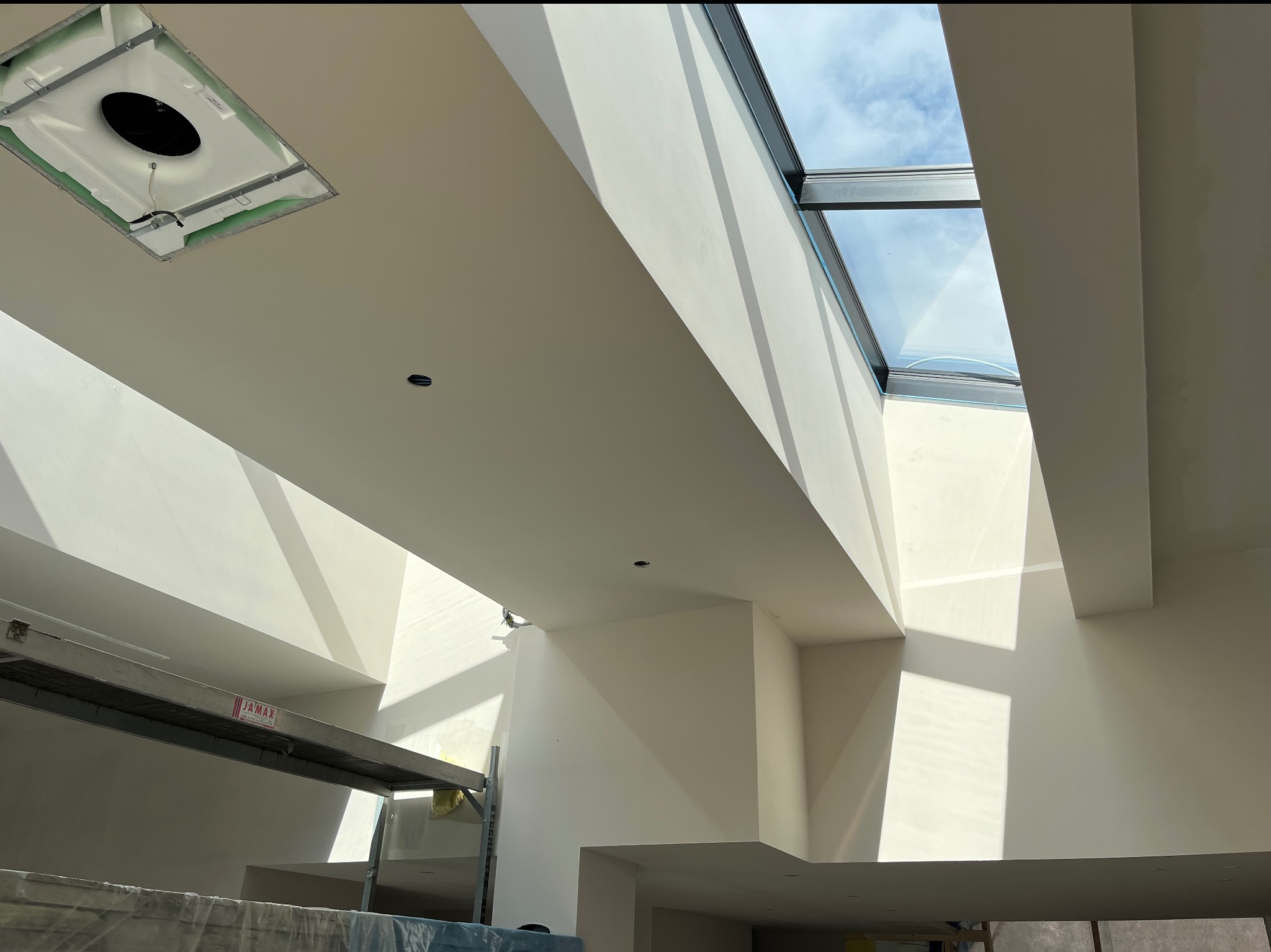 Wysokie wnętrze w trakcie wykańczania z widocznym rusztowaniem, oknem dachowym i przygotowanym otworem na oświetlenie sufitowe, ściany pokryte gładzią.