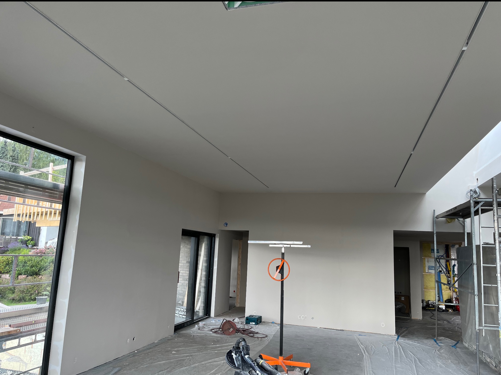 Wnętrze w trakcie prac wykończeniowych: ściany i sufit po szpachlowaniu, przygotowane do malowania, widoczny podnośnik do płyt oraz szlifierka do gipsu