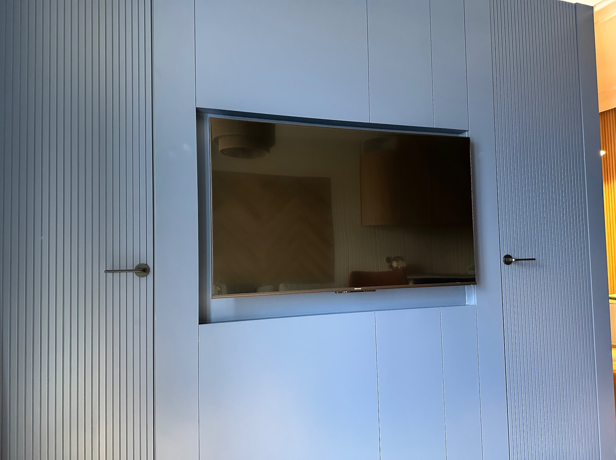 Niebieska szafa na wymiar z telewizorem wbudowanym w centralną część, drzwi z pionowymi frezowaniami i minimalistycznymi uchwytami.