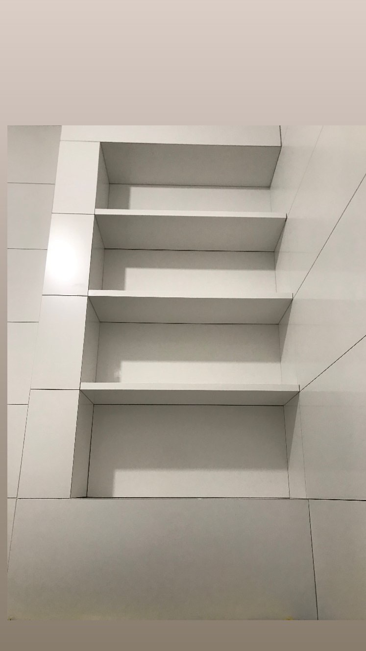 Wnęka z trzema białymi półkami, wykończona białymi płytami, widoczne subtelne linie fug.