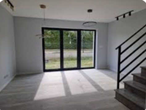 Jasne wnętrze z szarymi ścianami, ciemną stolarką okienną i schodami z czarną balustradą, oświetlone nowoczesnymi lampami wiszącymi.