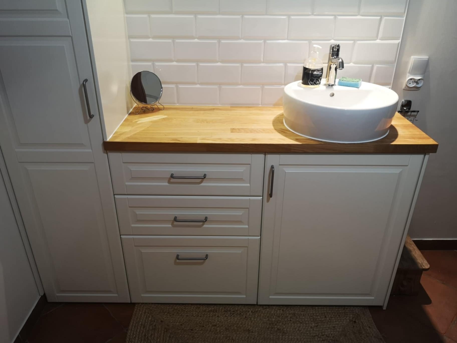 Biała umywalka nablatowa na drewnianym blacie w łazience we Wtórku, z białymi płytkami na ścianie i szafką z szufladami.