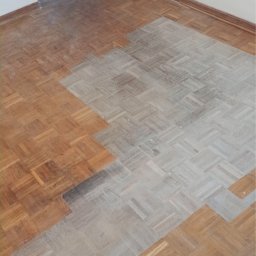 FLEX PATRYK WOJDAK - Parkiet ułożony w jodełkę, częściowo wyszlifowany i przygotowany do dalszej obróbki, widoczna różnica w kolorze i strukturze drewna przed i po szlifowaniu.