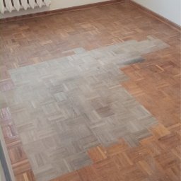 FLEX PATRYK WOJDAK - Parkiet po częściowym cyklinowaniu, z widoczną różnicą w kolorze i strukturze drewna, ukazującą efekt odświeżenia podłogi w pokoju z grzejnikiem.