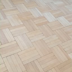 FLEX PATRYK WOJDAK - Częściowo odnowiona parkietowa podłoga w Warszawie, ukazująca różnicę w kolorze i wyglądzie przed i po zabiegu szlifowania.