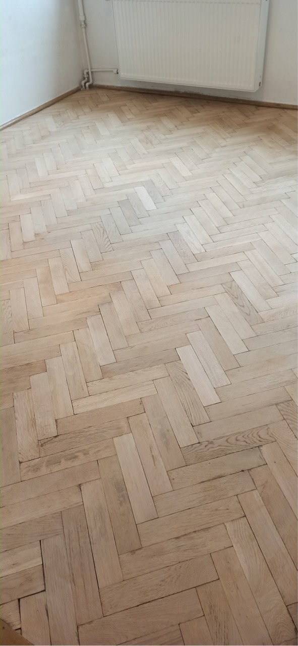 Parkiet ułożony w jodełkę, po renowacji, jasne drewno, widoczne grzejnik i fragment ściany