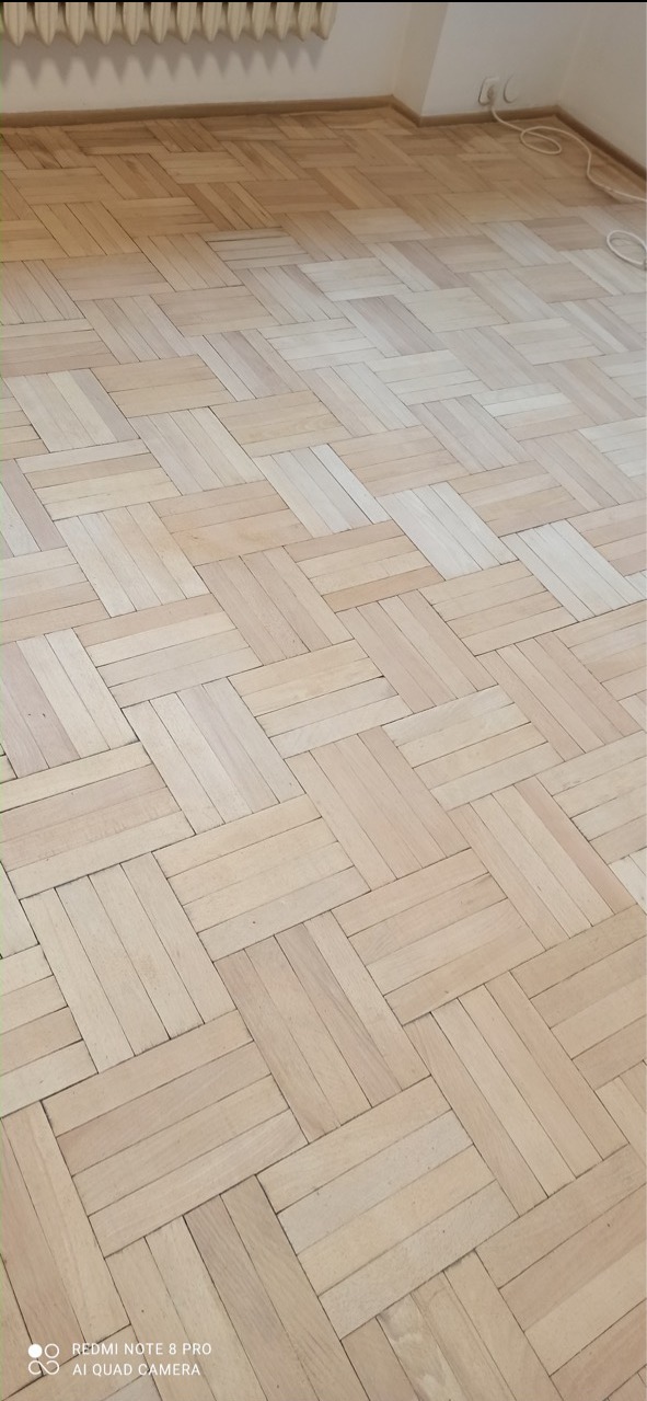 Częściowo odnowiona parkietowa podłoga w Warszawie, ukazująca różnicę w kolorze i wyglądzie przed i po zabiegu szlifowania.