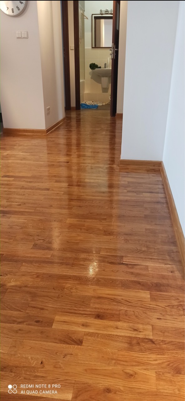 Wycyklinowana i polakierowana podłoga parkietowa w korytarzu mieszkania, widok w kierunku otwartych drzwi do łazienki.