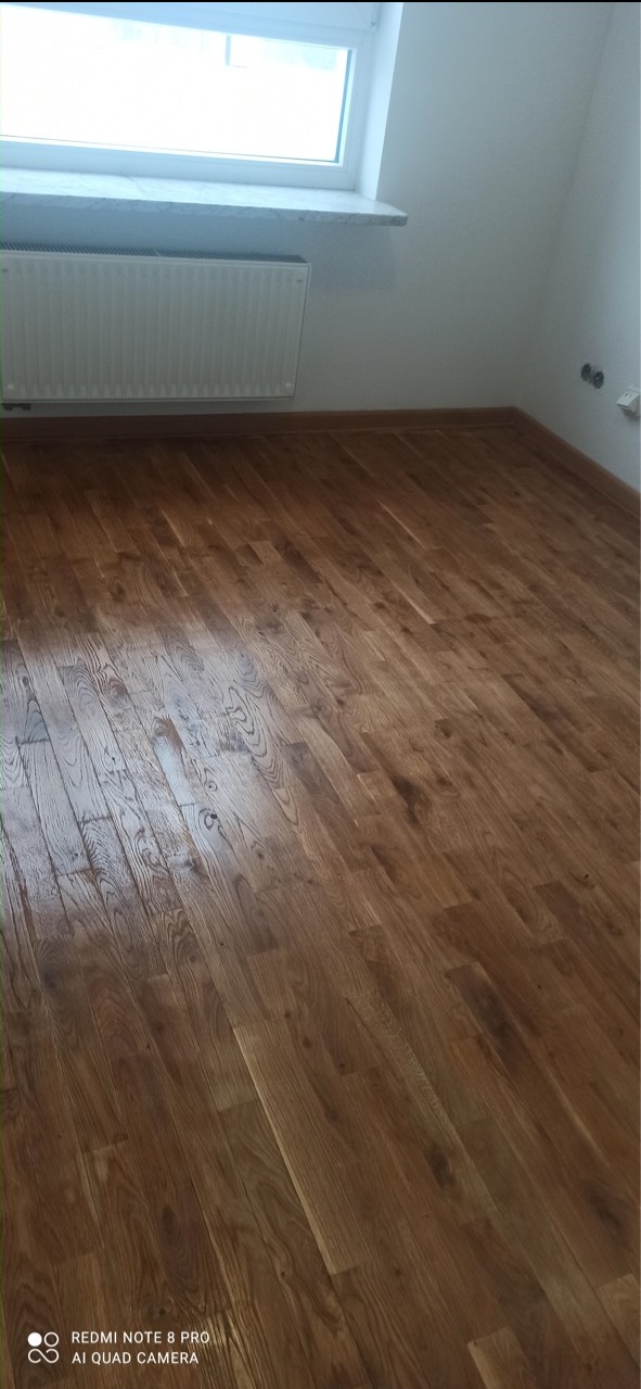 Wycyklinowana podłoga parkietowa z widocznym grzejnikiem i oknem w jasnym pomieszczeniu.