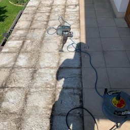 Grzegorz Tomasiak GT-BAU - Demontaż starej posadzki na balkonie za pomocą młota udarowego. Częściowo usunięte płytki, widoczny kabel zasilający i cień osoby wykonującej prace.