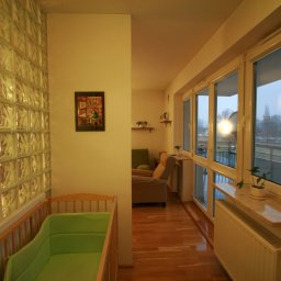 BARTŁOMIEJ ONDRUCH - Umeblowane mieszkanie 36m2 po remoncie: pokój dziecięcy z łóżeczkiem, ściana z luksferów, widok na salon i balkon z roślinami w doniczkach na parapecie.