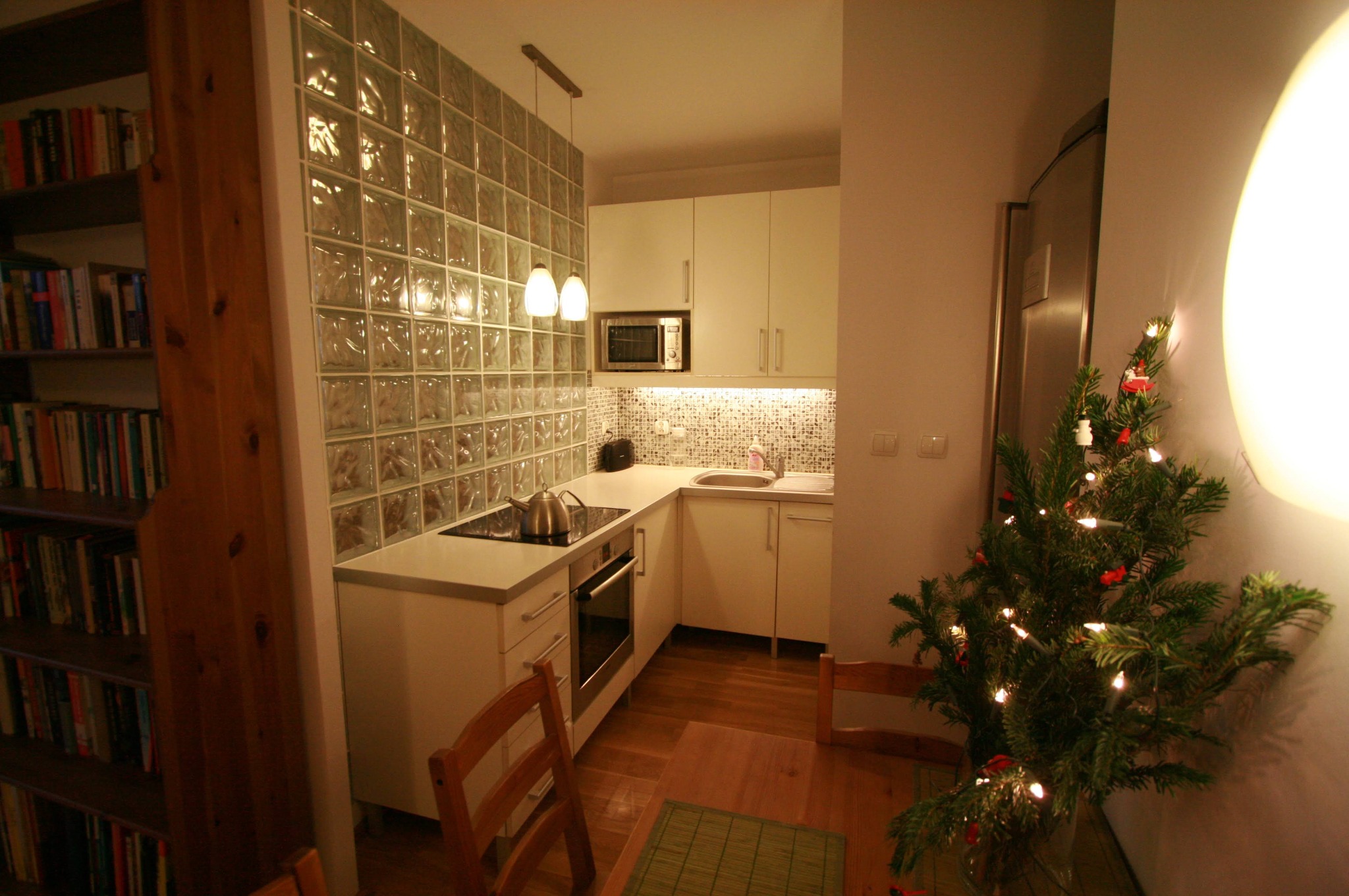 Umeblowana kuchnia w mieszkaniu o powierzchni 36m2, oddzielona od reszty pomieszczenia ścianką z luksferów. Widoczny stół z krzesłami i mała choinka.
