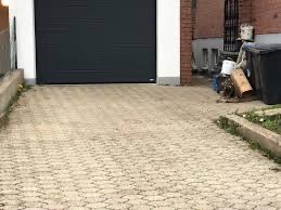 Ułożona kostka brukowa na podjeździe przed garażem, widoczne ślady zabrudzeń i resztki materiałów budowlanych po bokach.