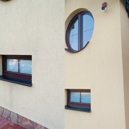RClean - Elewacja budynku przed i po czyszczeniu, widoczne różnice w kolorze i czystości tynku, okrągłe okno, kamera monitoringu.