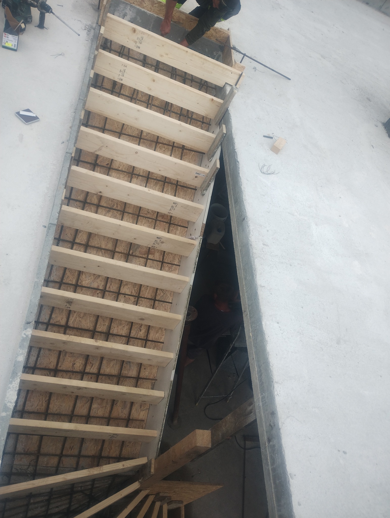 Formowanie schodów żelbetowych z drewnianym szalunkiem i zbrojeniem stalowym, widok z góry na placu budowy.