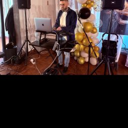 Seb Records - DJ z brodą i okularach gra na keyboardzie Recordbox na tle dekoracji z białych i złotych balonów oraz dwóch głośników JBL podczas imprezy.