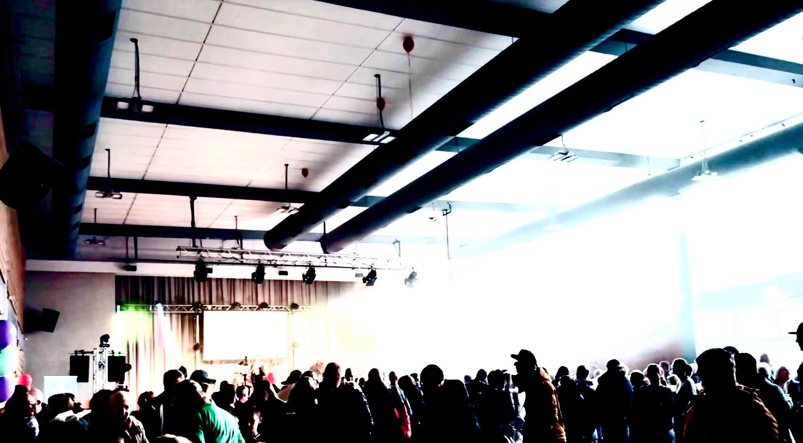 Tłum ludzi obserwujących scenę z oświetleniem i ekranem podczas wydarzenia w hali.