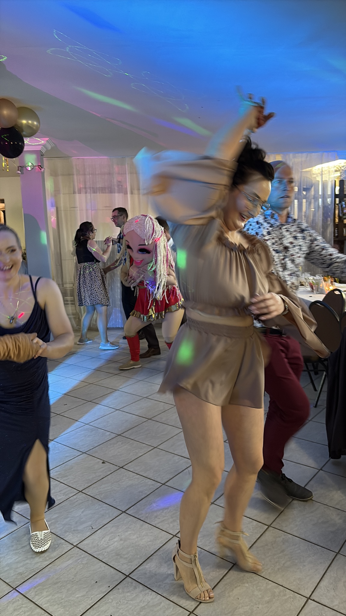 Roztańczona impreza integracyjna w Kołobrzegu, z osobą w masce, podświetlona kolorowymi światłami, tworząca radosną atmosferę.