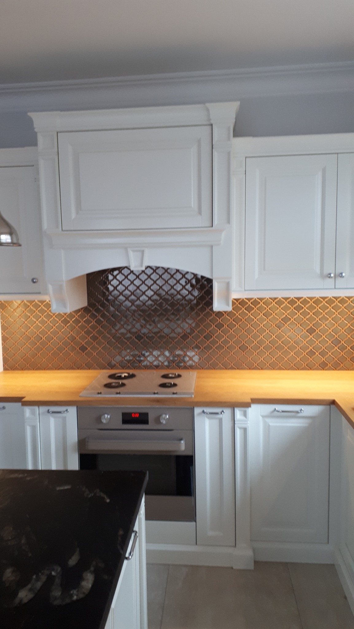 Wykończona kuchnia z białymi szafkami, drewnianym blatem i mozaiką w odcieniach brązu nad płytą grzewczą i piekarnikiem.