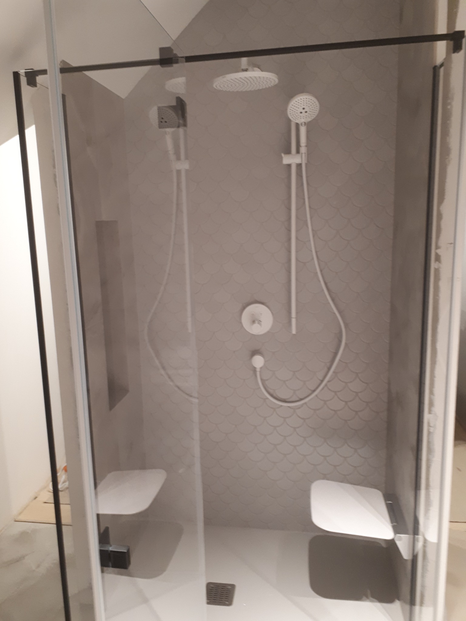 Nowoczesna kabina prysznicowa z dwoma siedziskami, deszczownicą i słuchawką, wykończona płytkami w kształcie rybiej łuski.