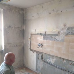 Regameh - Demontaż płytek w kuchni w Dongen, widoczny fragment instalacji wodnej i resztki kleju na ścianie, przygotowanie do dalszych prac remontowych.