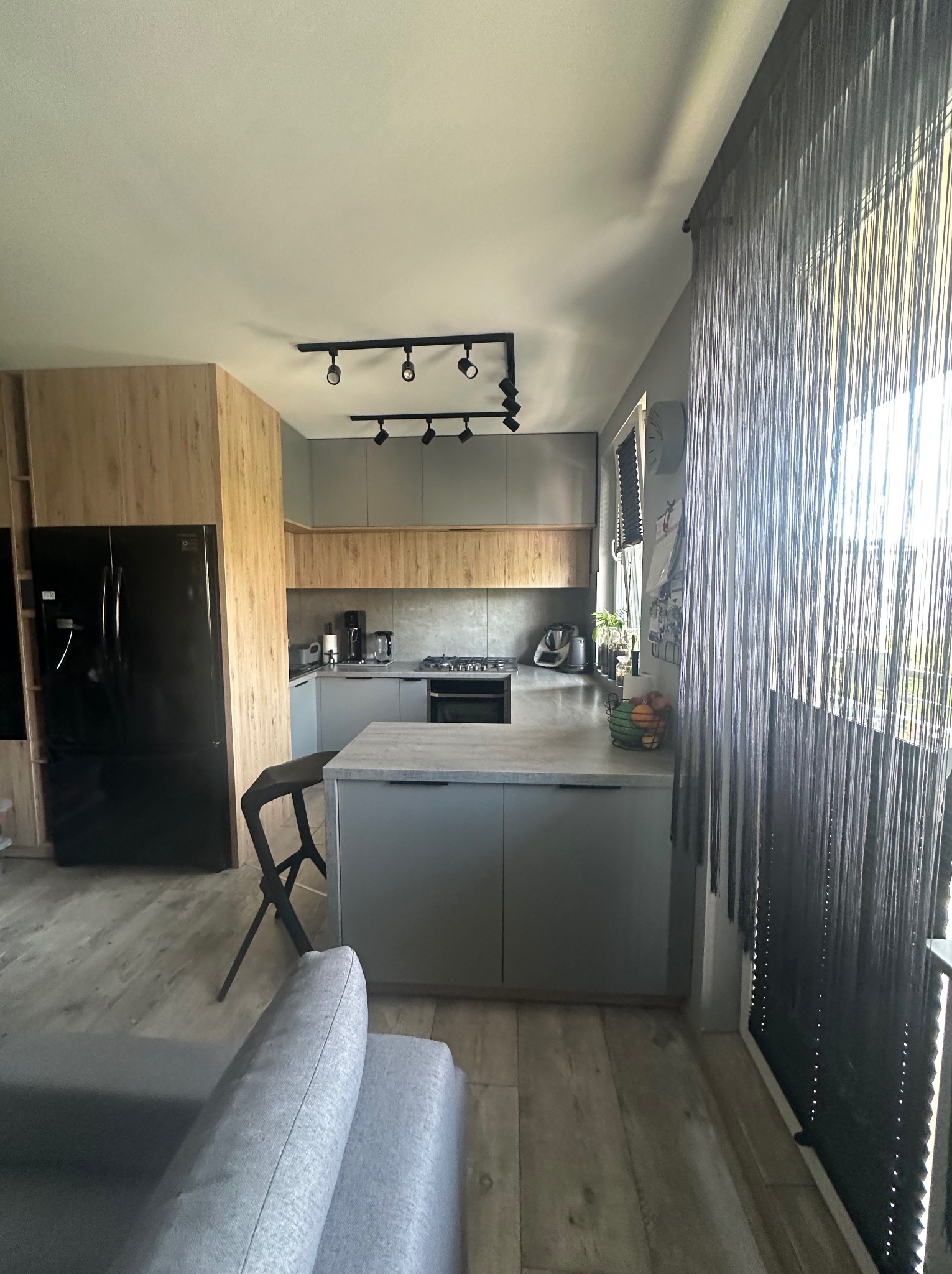 Nowoczesna kuchnia z wyspą i drewnianymi akcentami w Gorzowie Wielkopolskim. Czarny sprzęt AGD i szare szafki tworzą elegancką przestrzeń.