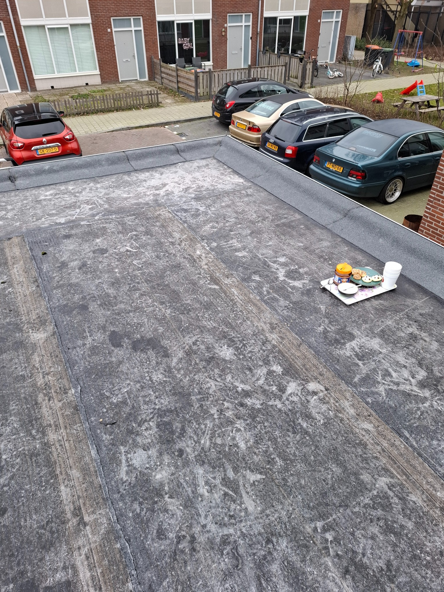 Widok z góry na płaski dach pokryty papą w Katowicach, z widocznymi śladami użytkowania i niedawnym poczęstunkiem na tacy: ciastka, napój i puste kubki.