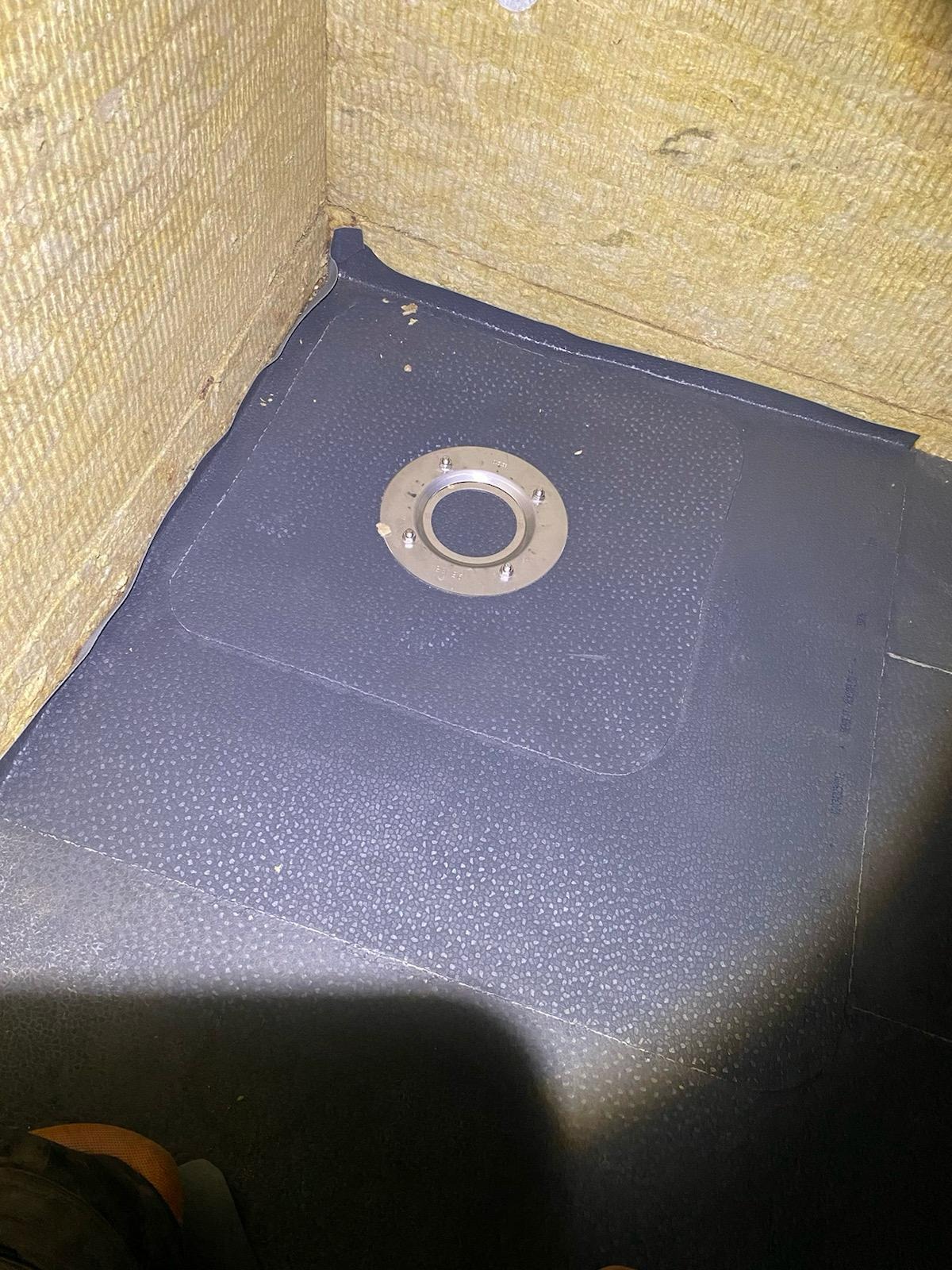 Szczelna hydroizolacja z wpustem podłogowym w rogu pomieszczenia, ściany wyłożone wełną mineralną. Detal wykończenia w trakcie prac.