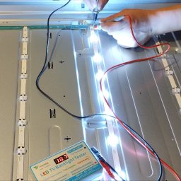 SAT-ANT - Testowanie podświetlenia LED telewizora za pomocą testera z wyświetlaczem 18.3V, widoczne paski LED z włączonymi diodami i ręka technika przykładająca sondę pomiarową.